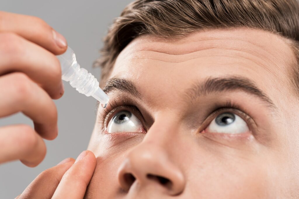 cropped view of young man applying eye drops isolated on grey