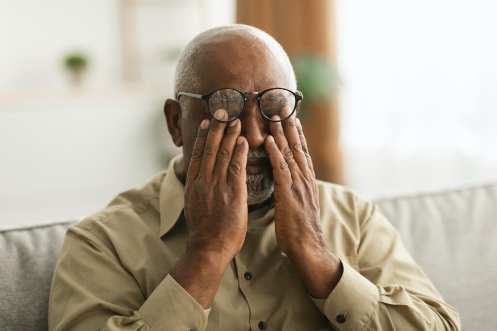 Senior African Man Rubbing Eyes Wearing Eyeglasses Having Glaucoma Indoors