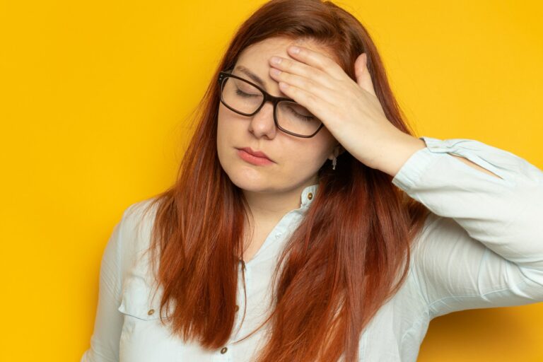 Worker young woman in shirt and eyesight glasses with headache on yellow wall background. Stress
